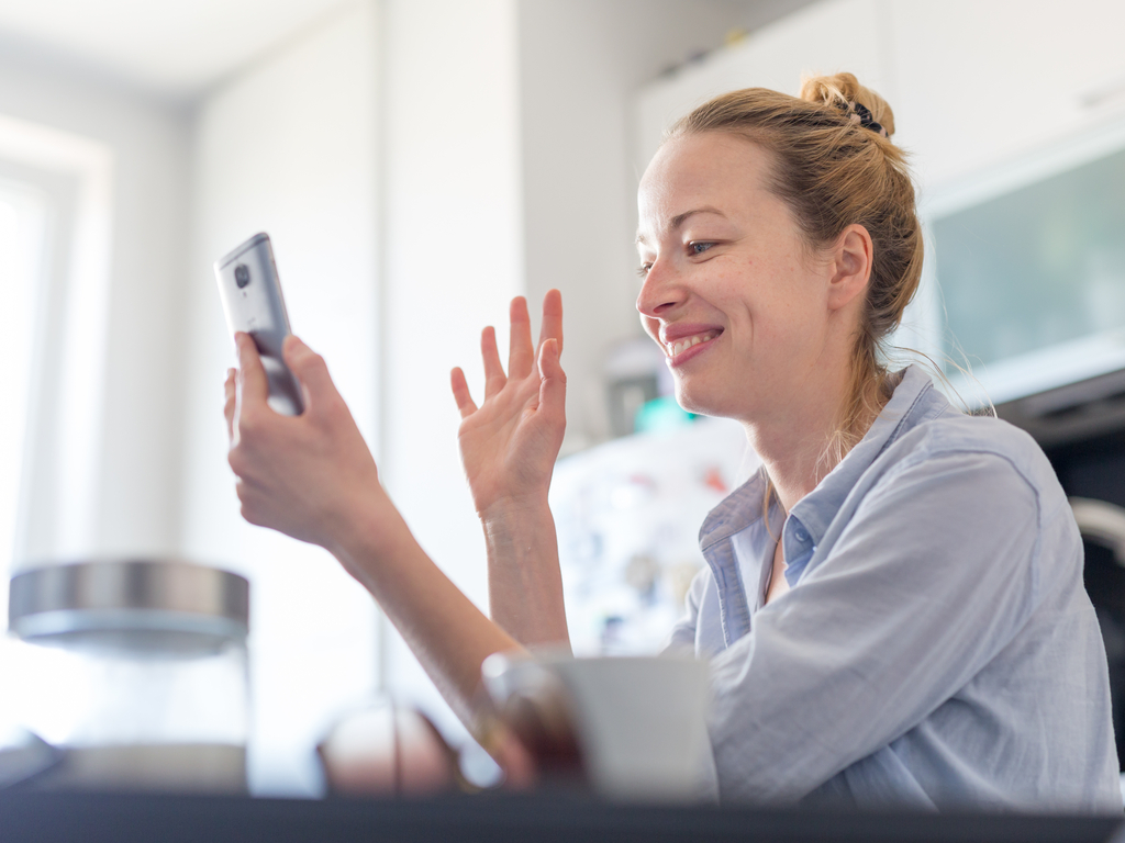 Business woman waves via video chat as she socially distances